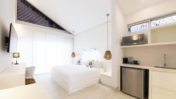 A modern bedroom with a large bed, bedside tables, a built-in TV, and a compact kitchen area with a microwave.