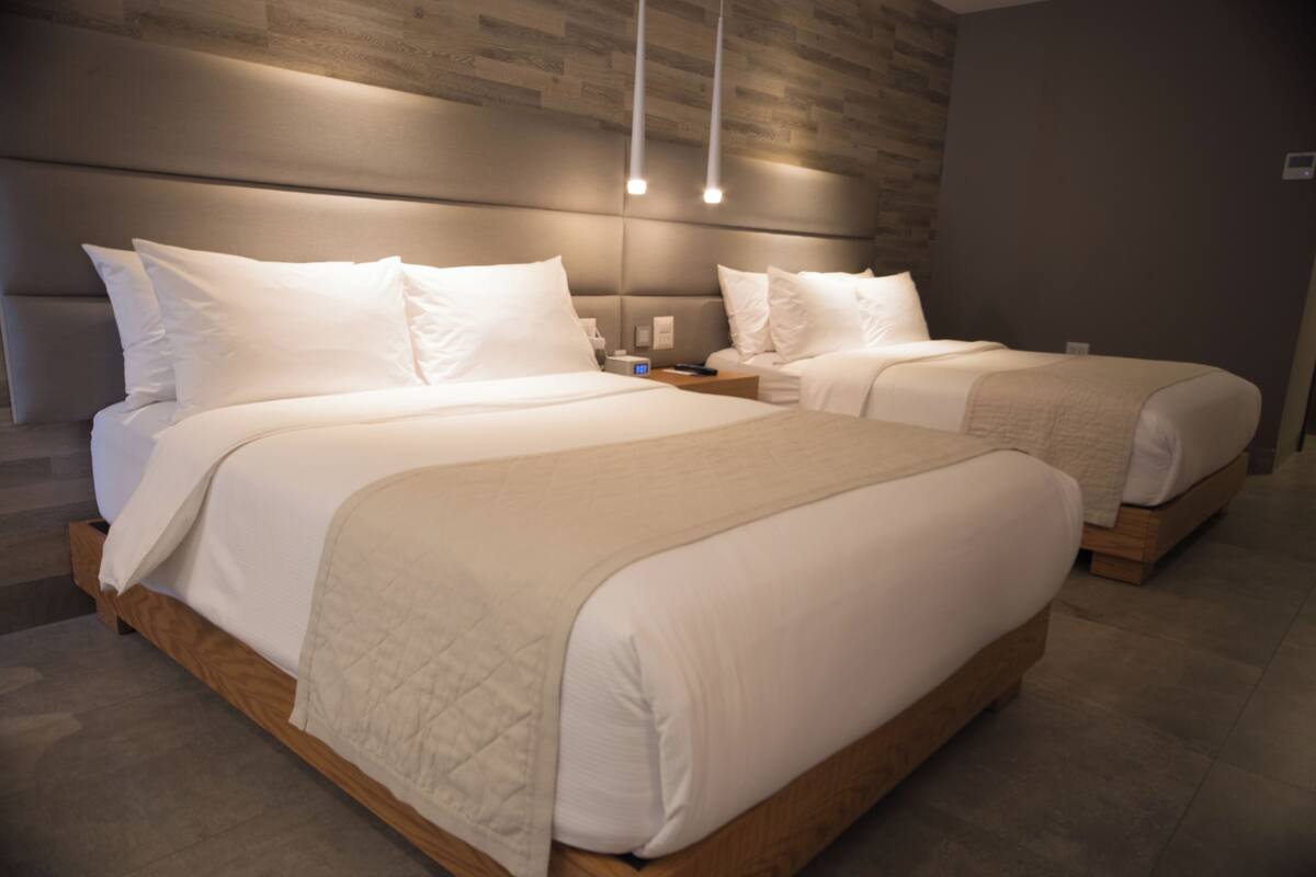 Habitación de hotel con dos camas, cabecera de madera y lámpara moderna.