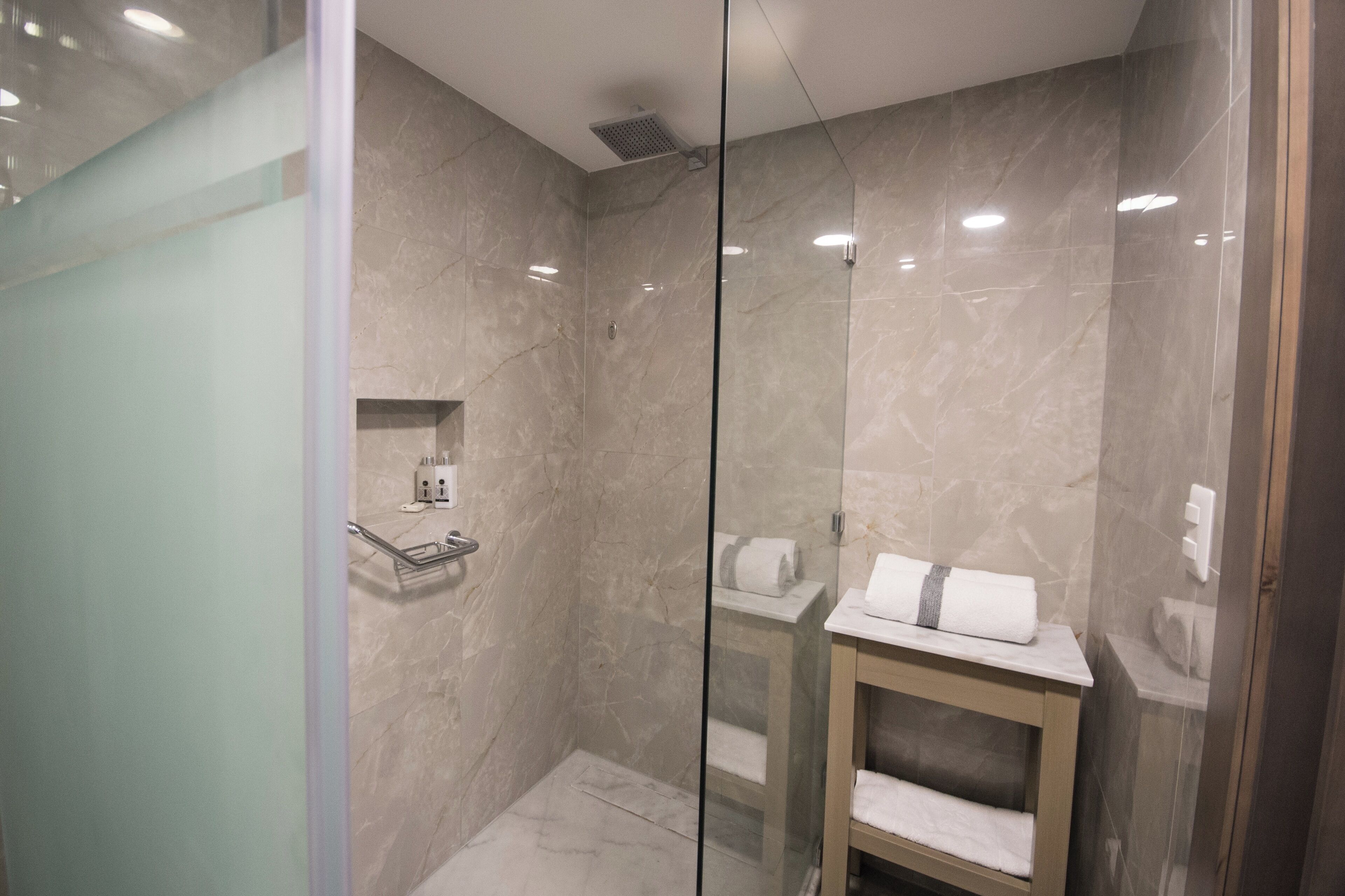 Un baño moderno con ducha de vidrio, paredes de mármol y tocador de madera con toallas.