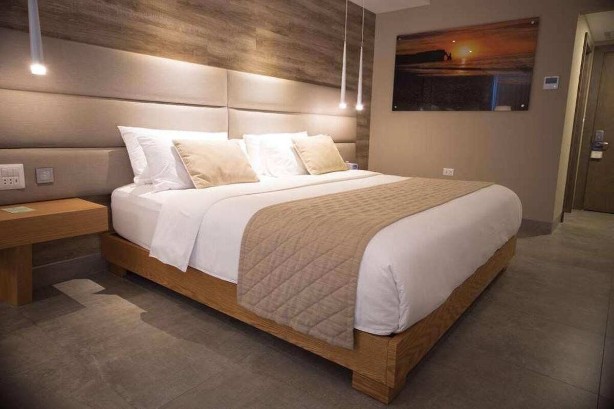 Una habitación de hotel moderna con una cama grande, cabecera de madera y un cuadro en la pared.