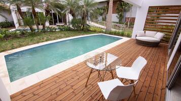 Una zona junto a la piscina con una terraza de madera, una mesa de vidrio con sillas y un sofá blanco.