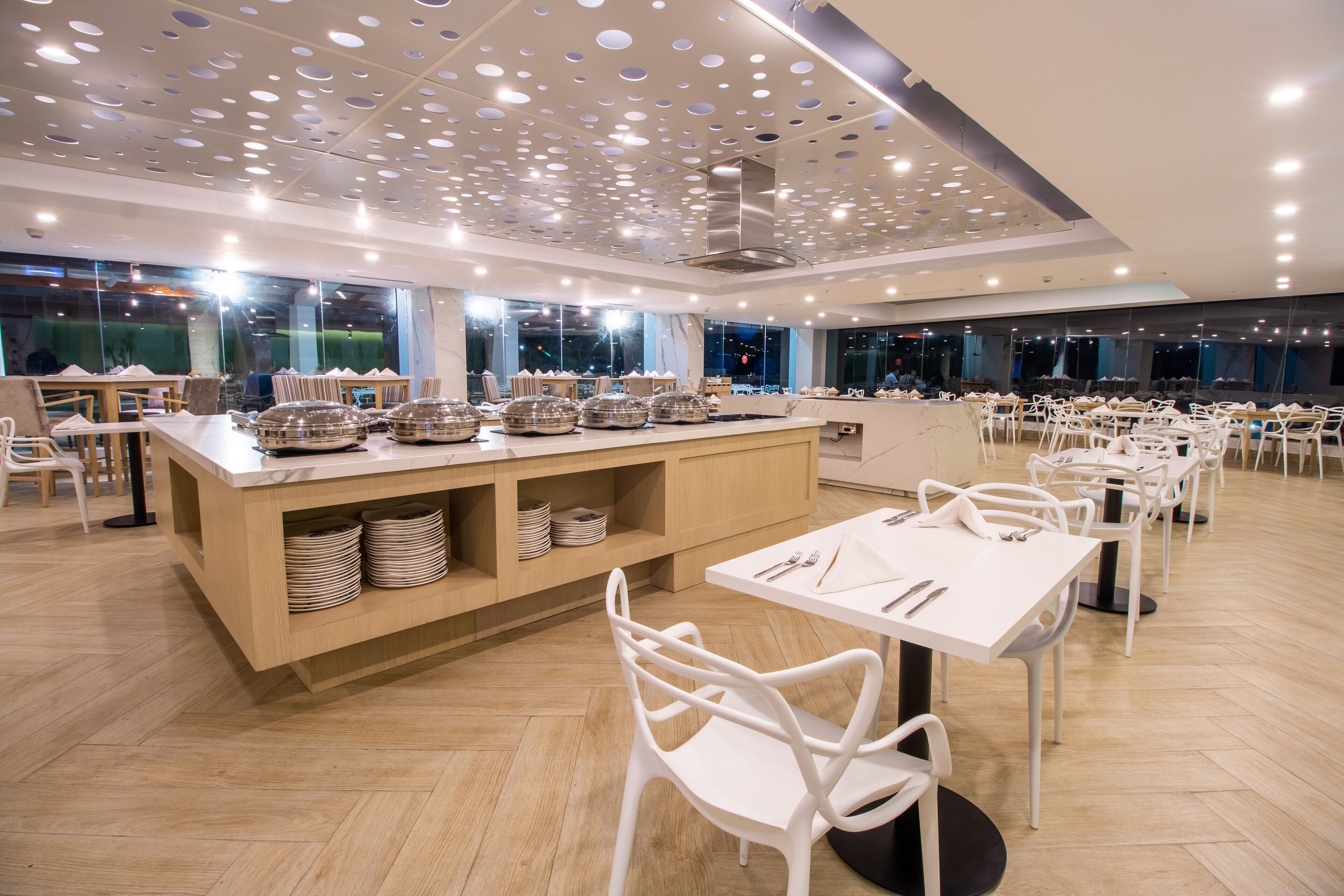 A modern dining area with white chairs, a central island with dishes, and a ceiling with circular patterns.
