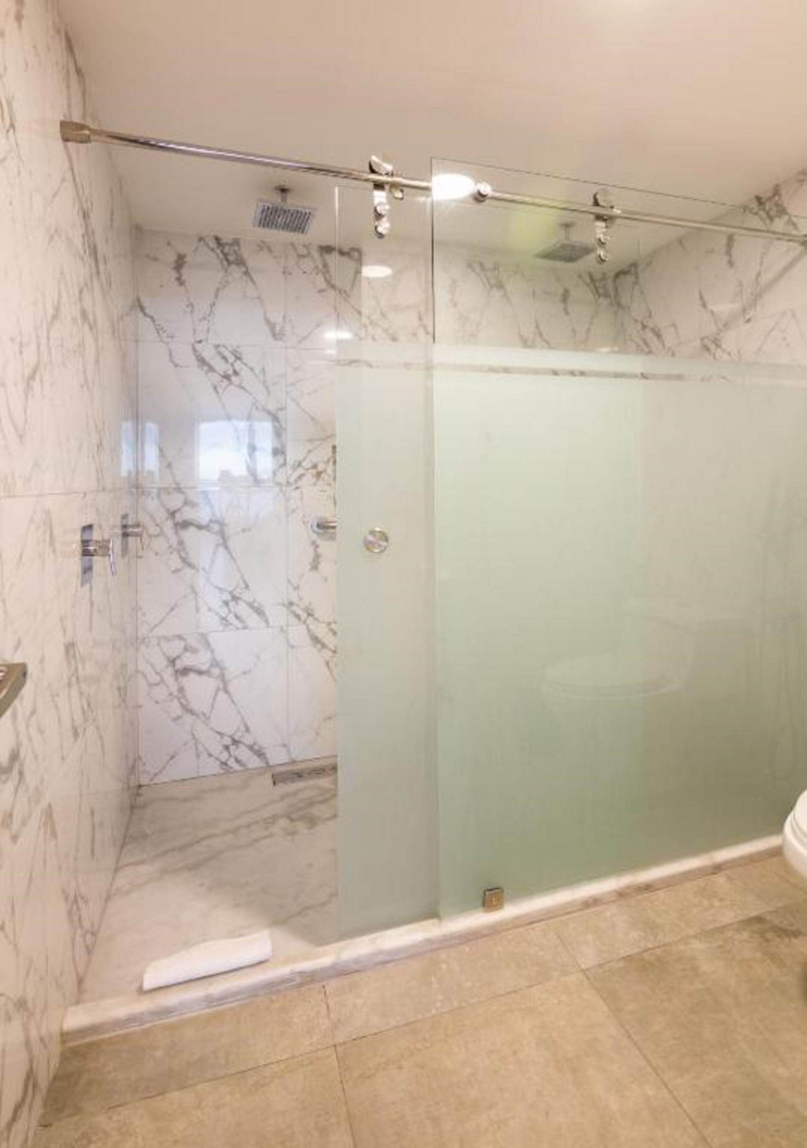 A glass-enclosed shower with marble walls and a tiled floor.