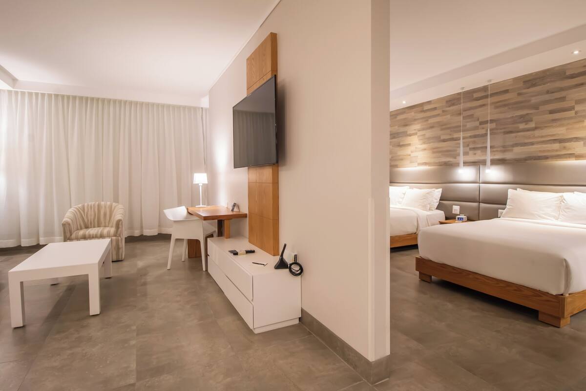 Habitación de hotel moderna con televisión de pantalla plana, escritorio, silla, cama y un panel de madera decorativo.