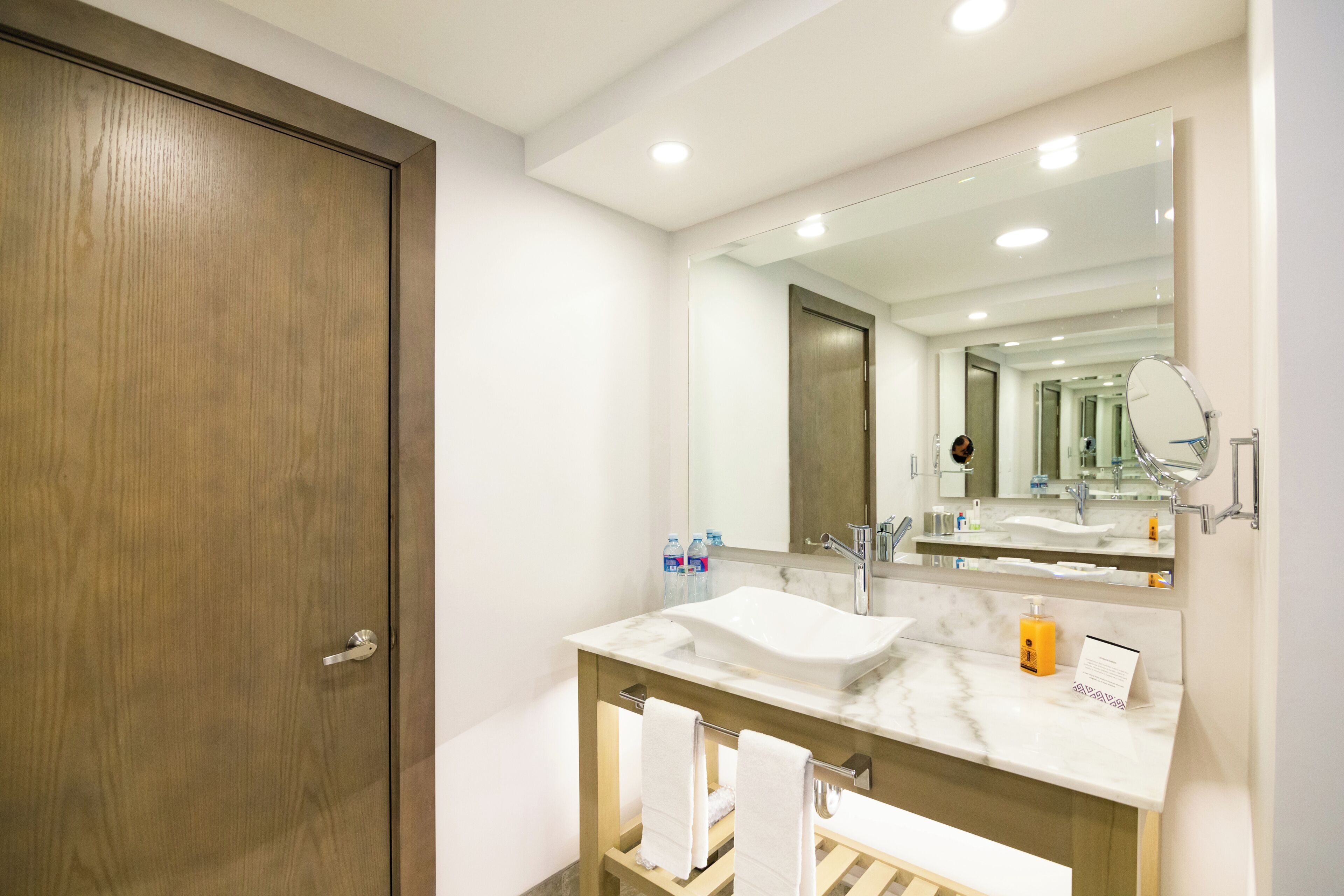 A modern bathroom with a wooden door, a large mirror, a marble sink, and a towel rack.