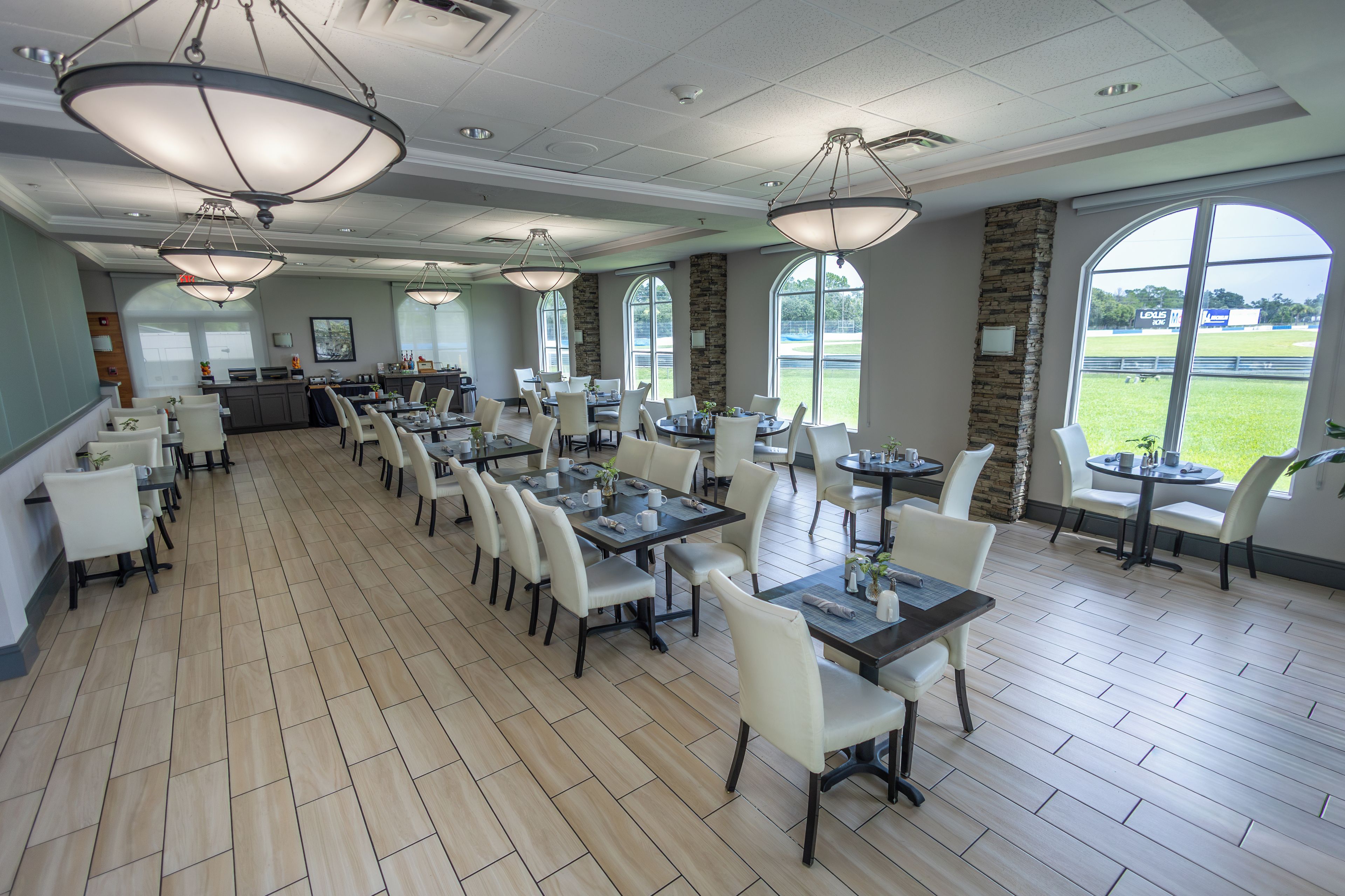 A spacious dining area with multiple tables and chairs, large windows offering views of a baseball field, and a stone accent wall.