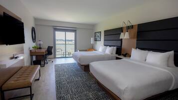 Een hotelkamer met twee bedden, een bureau, een stoel, een televisie en een balkon.