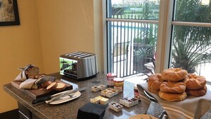 A kitchen counter with a toaster, bread, pastries, condiments, and utensils.