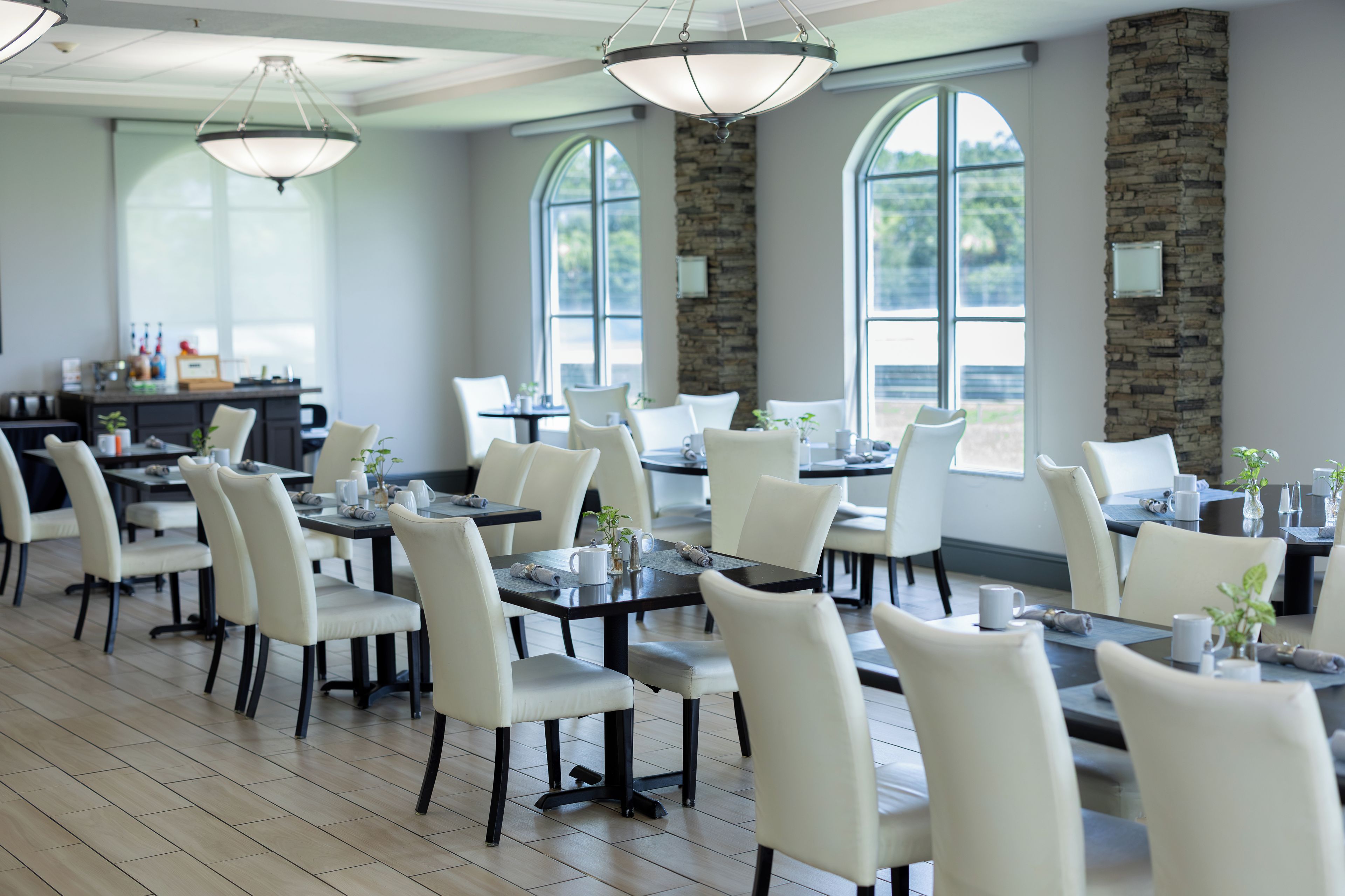 A spacious dining area with multiple tables and chairs, large windows, and a stone accent wall.