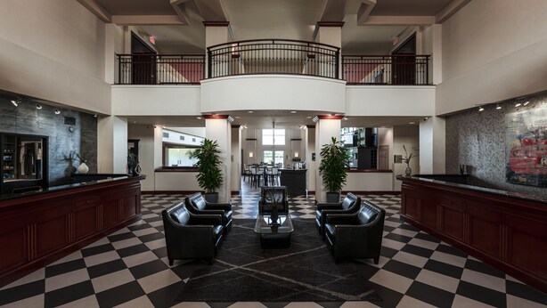 A spacious lobby with a checkered floor, a central seating area, and a high ceiling with a balcony.