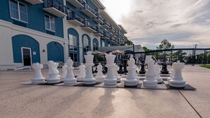 A large chessboard set up on a concrete surface in front of a hotel with blue and white exterior walls and balconies.