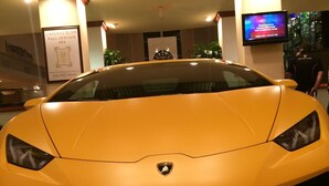 A Lamborghini with a black hood and yellow body, parked indoors with a checkered floor and a clock on the wall.