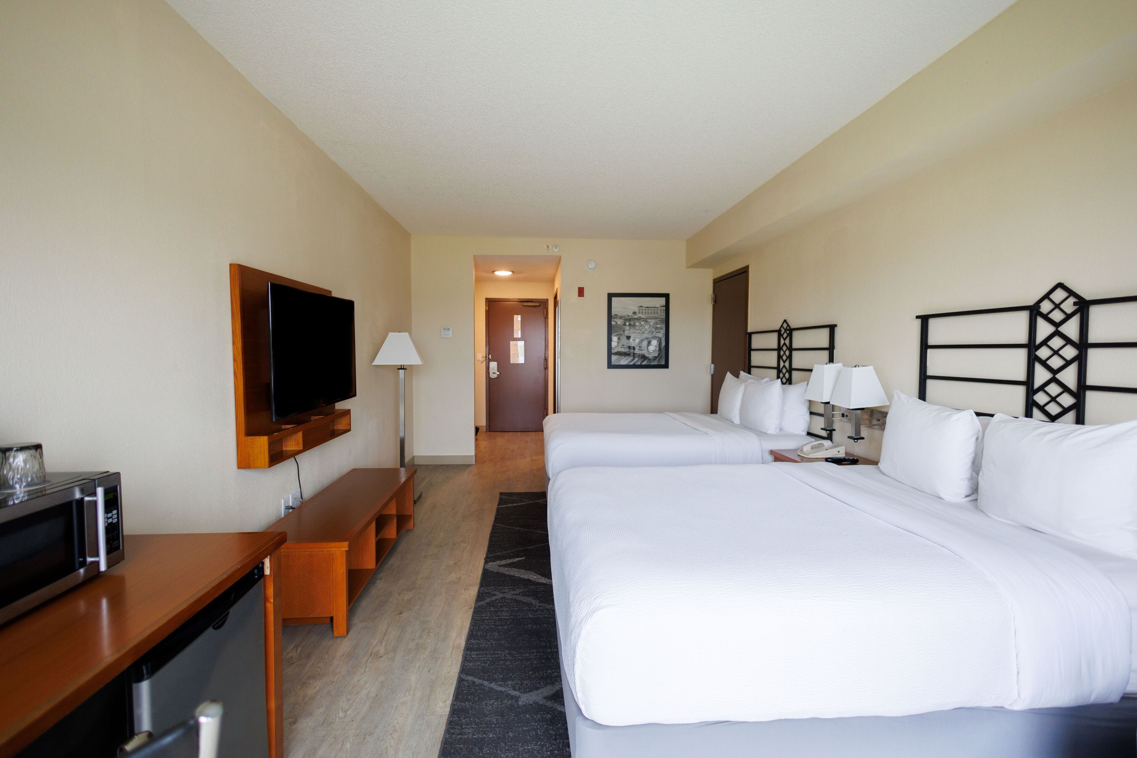 A hotel room with two beds, a TV, a desk with a microwave, and a bench.
