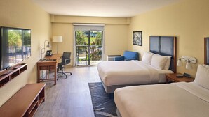 A hotel room with two beds, a desk, a chair, a TV, and a balcony with a view.