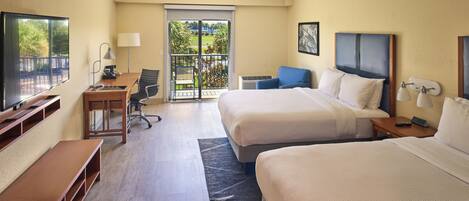A hotel room with two beds, a desk, a chair, a TV, and a balcony with a view.