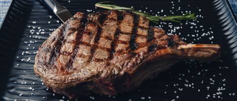 A grilled steak with a knife and a sprig of rosemary on a black plate.