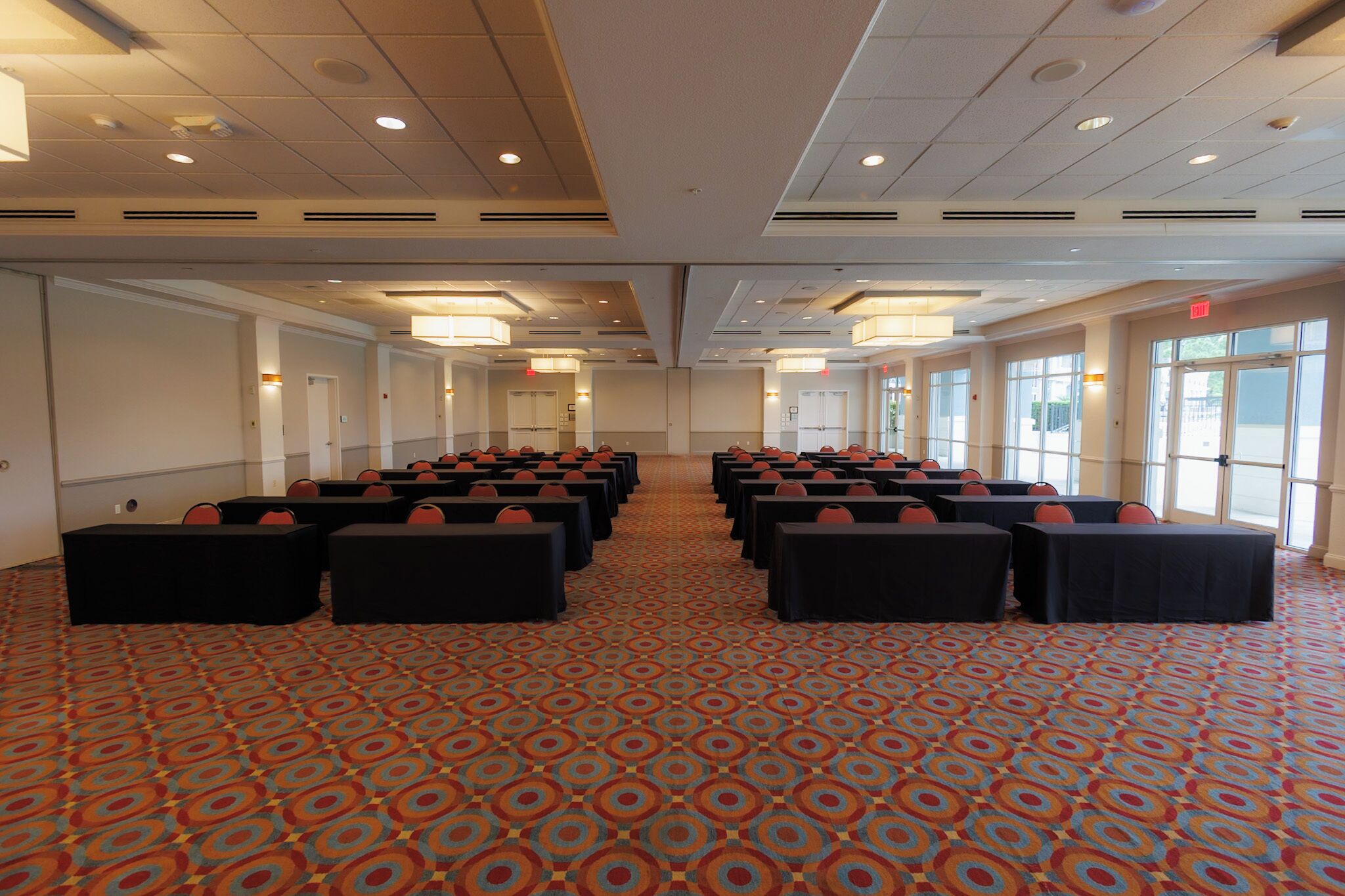 A conference room with rows of tables and chairs, large windows, and a patterned carpet.