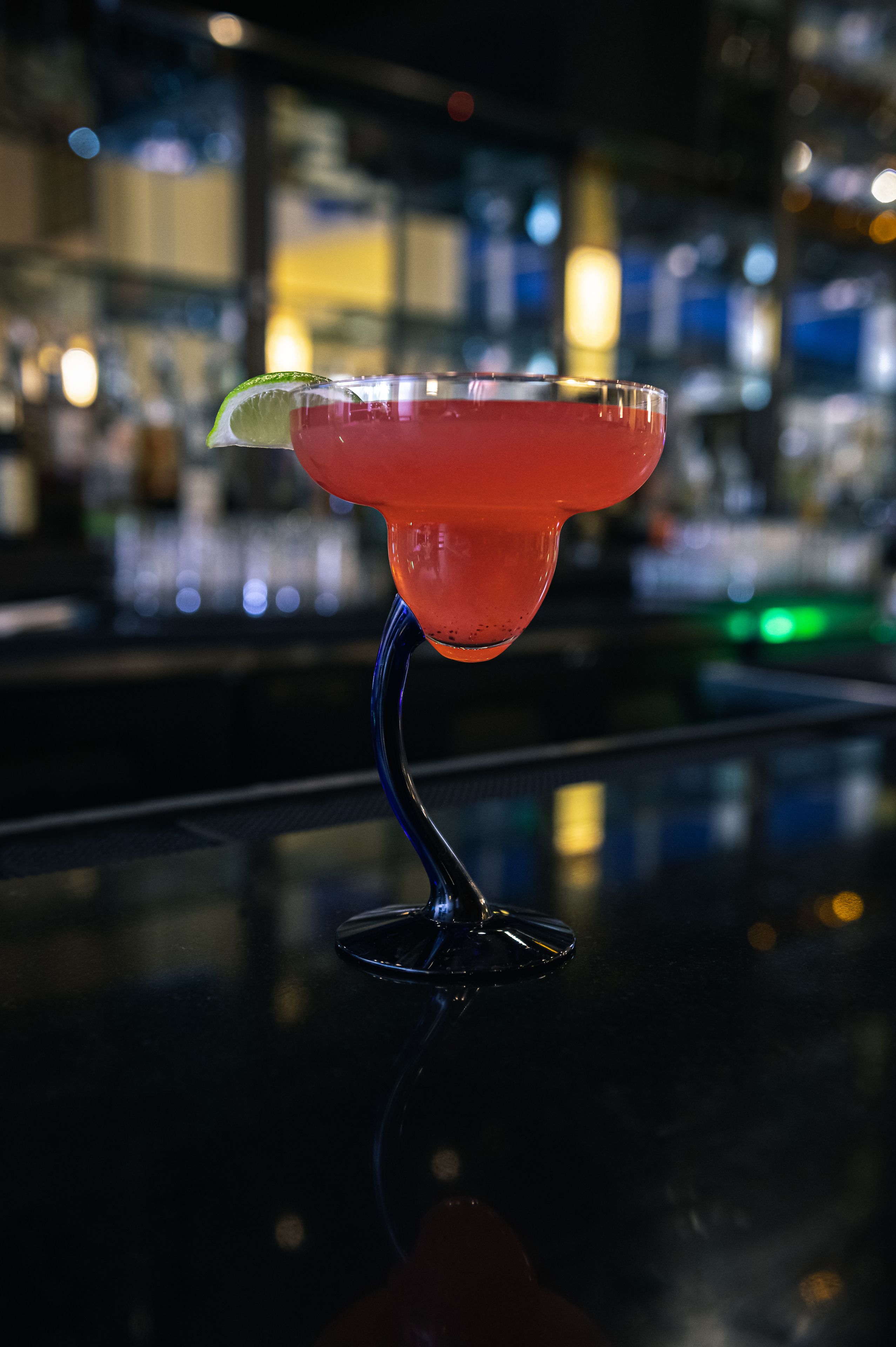 Een cocktail in een longdrinkglas met een limoen op een barkruk.