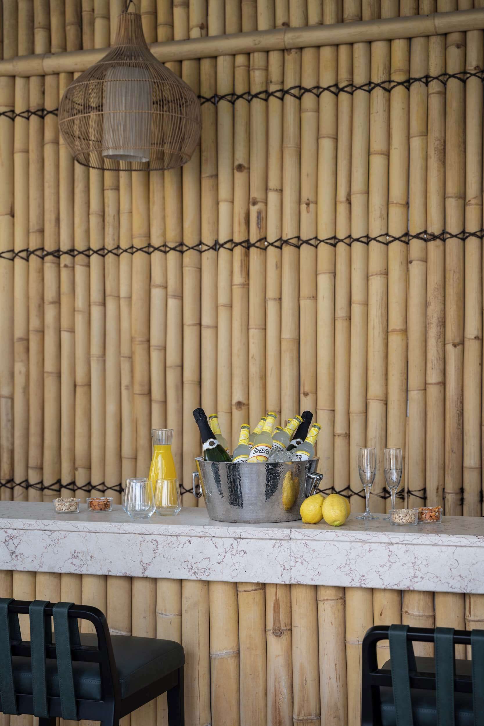 A bar area with a bamboo backdrop, a metal bucket with bottles, glasses, and lemons.