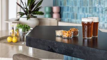 Zona de bar con mostrador negro, dos vasos de cerveza, un bol de aperitivos y una planta en maceta.