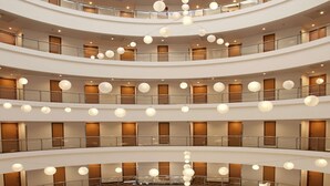 Un atrio de varios niveles con un espacio central abierto, múltiples balcones y luces esféricas colgantes.