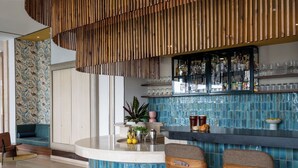 Un área de bar moderna con una barra curva, dos taburetes de madera y un revoque de azulejos azules.