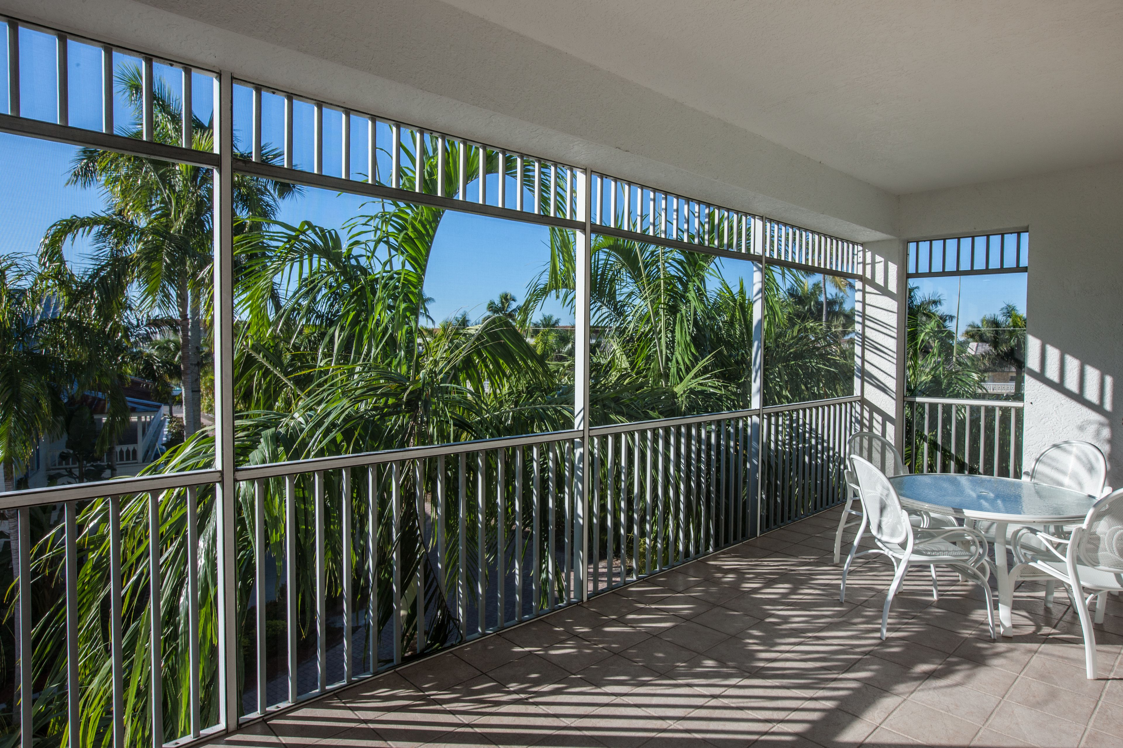 A balcony with a glass railing, white chairs, and a table.