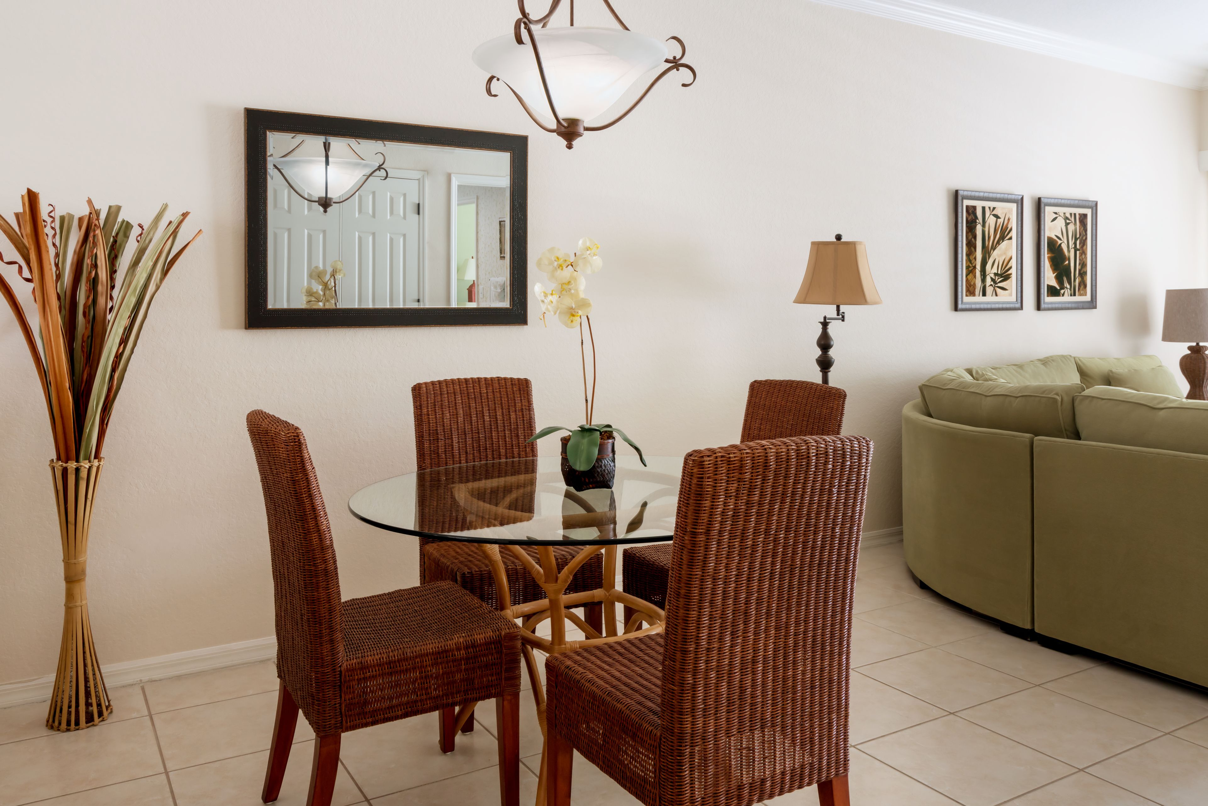 A dining area with wicker chairs, a glass table, and a vase with flowers.
