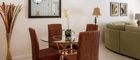 A dining area with wicker chairs, a glass table, and a vase with flowers.