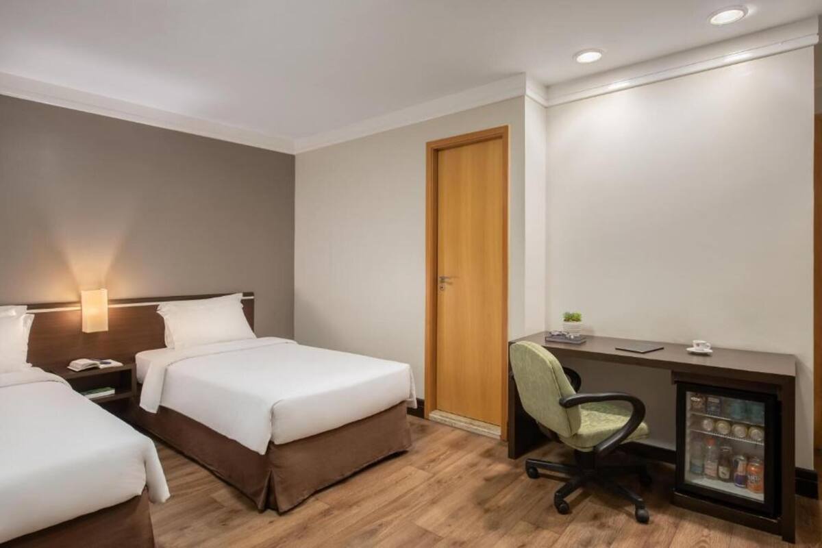 A hotel room with two beds, a desk with a computer, a chair, and a minibar.