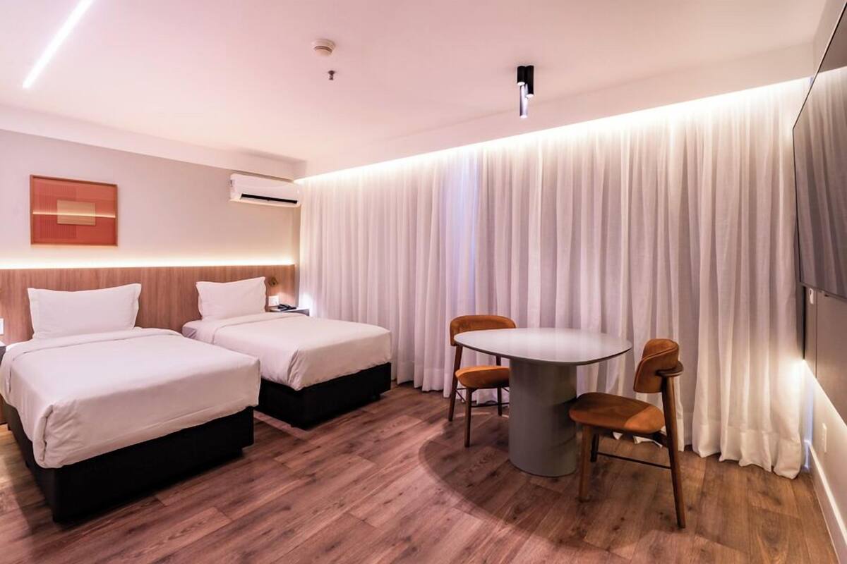 A hotel room with two beds, a round table, and a chair.