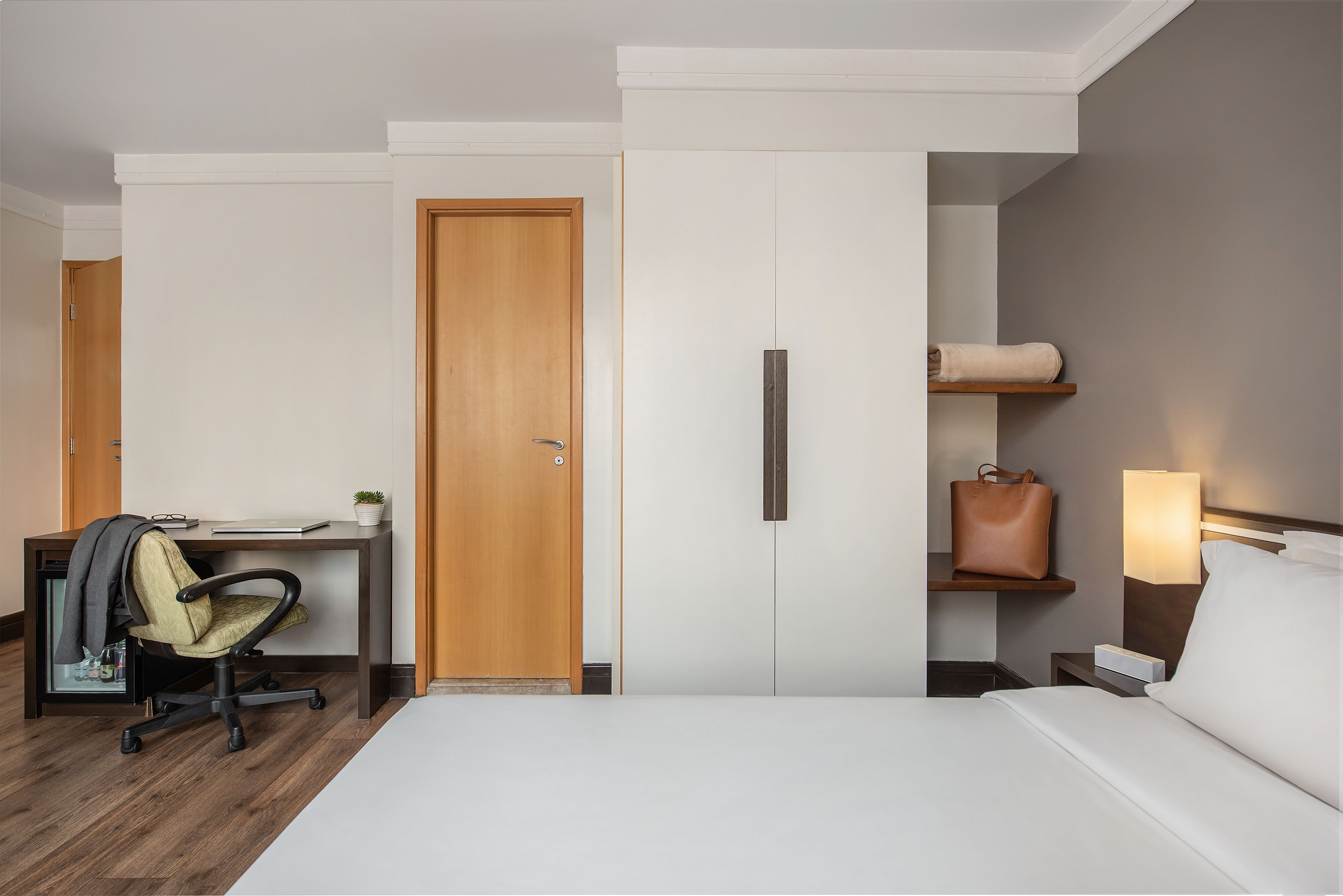 Una habitación de hotel con cama, escritorio, silla y mesita de noche con lámpara.