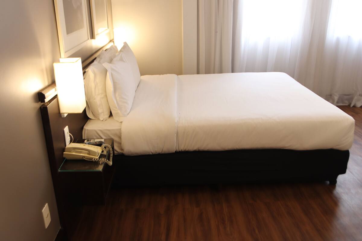 A hotel room with a large bed, white bedding, a bedside telephone, and a nightstand.