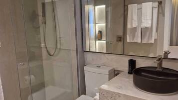 A modern bathroom with a glass-enclosed shower, a white toilet, a marble sink, and a mirror above the sink.