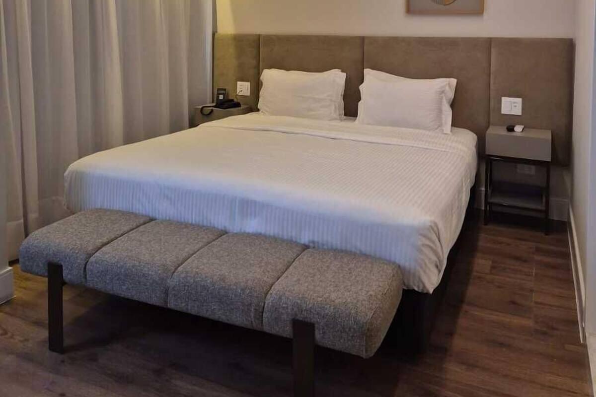 A modern bedroom with a large bed, a bench, a headboard, a bedside table, and a wall-mounted artwork.