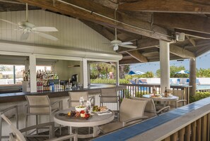 Un área de bar al aire libre con techo, asientos, piscina y vistas al exterior.