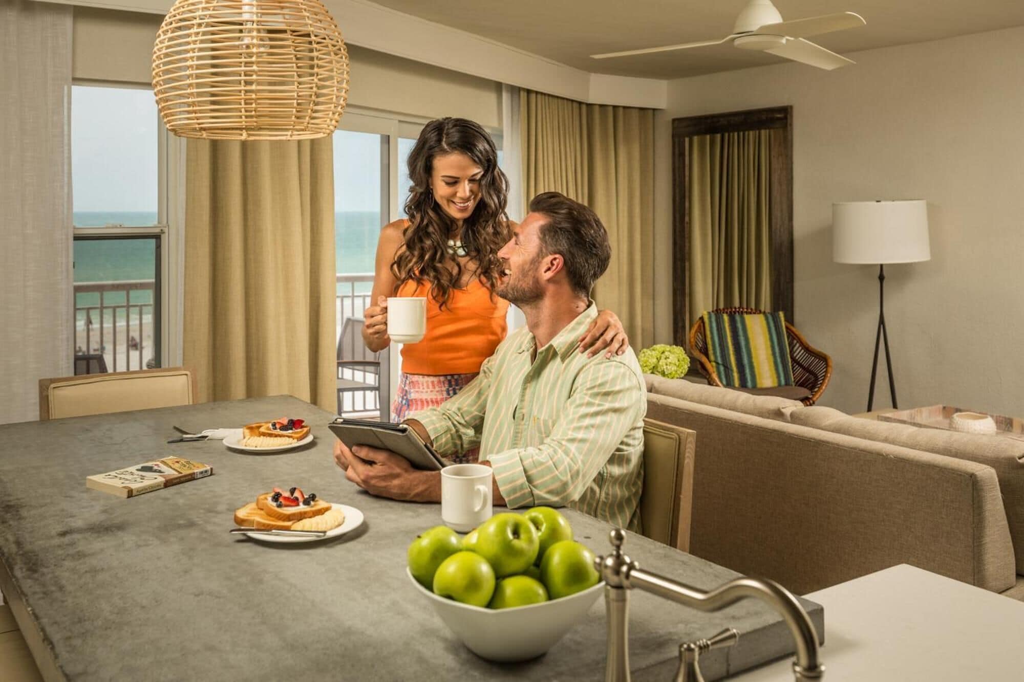 A hotel room with a dining area, a sofa, a chair, and a view of the sea.