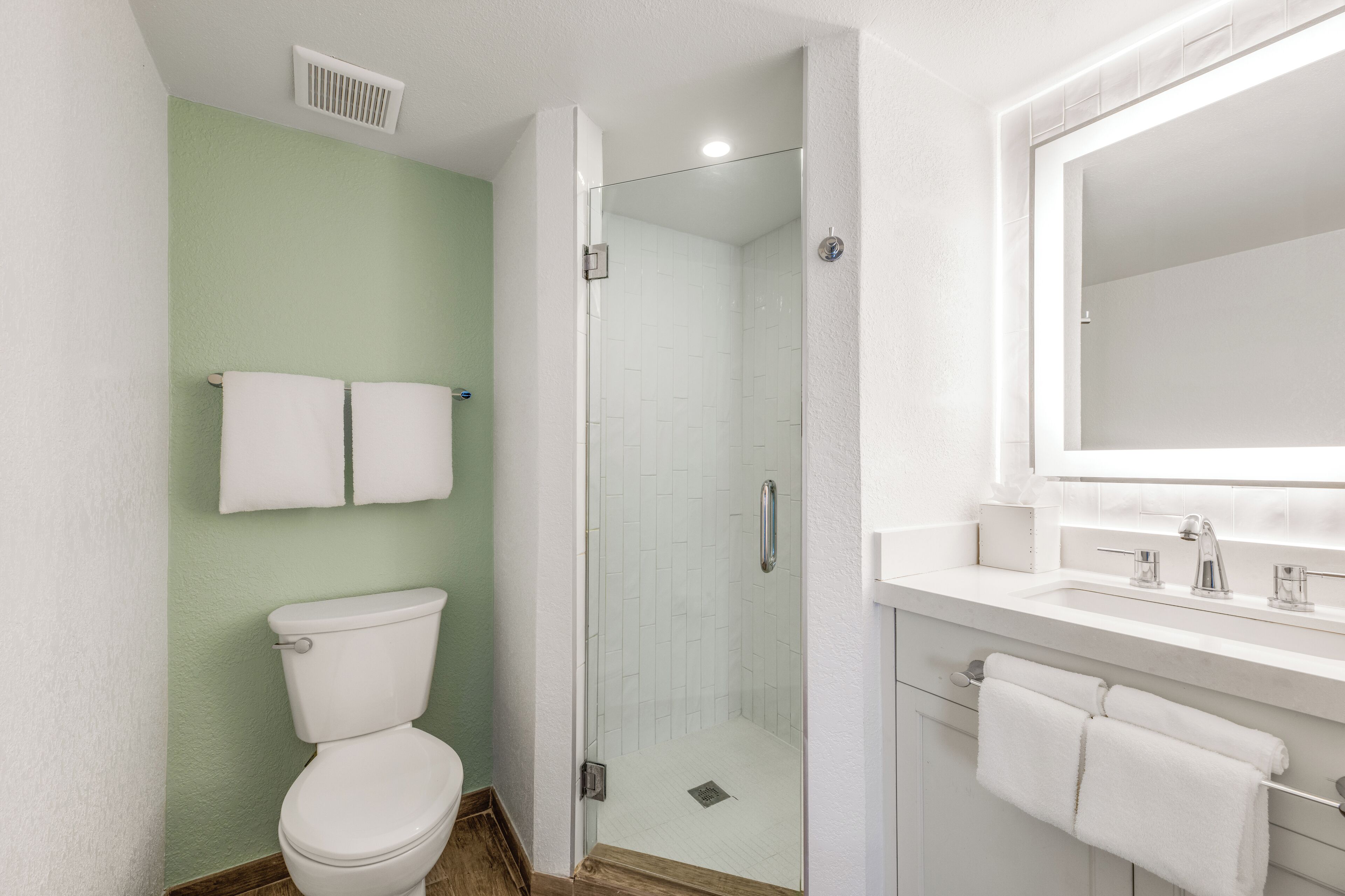 A bathroom with a toilet, a glass-enclosed shower, and a sink with a mirror.