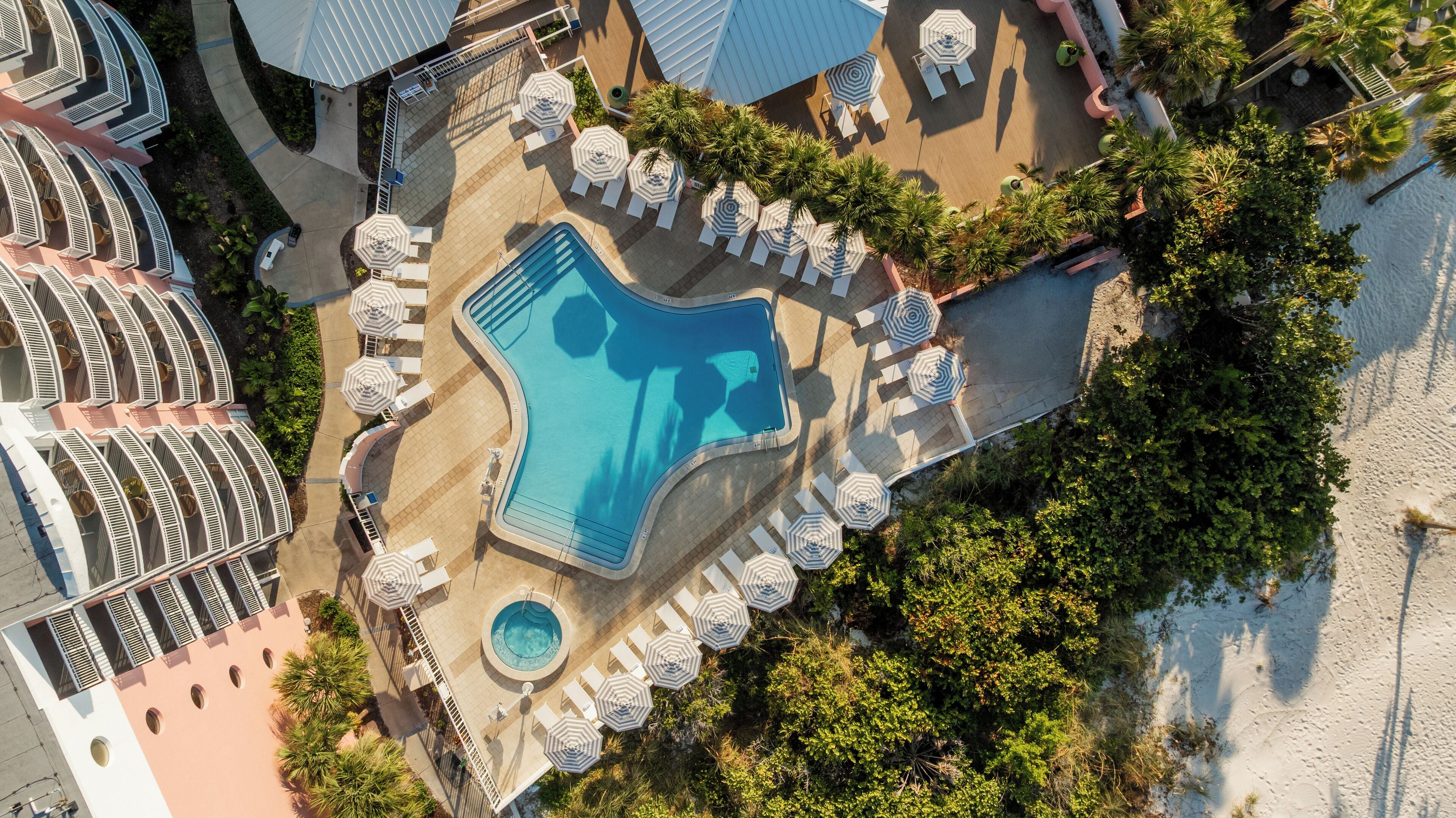 Eine Luftaufnahme eines Resorts mit Schwimmbad, Liegestühlen und Palmen.