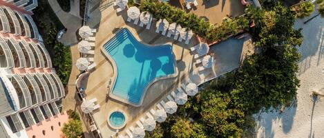Eine Luftaufnahme eines Resorts mit Schwimmbad, Liegestühlen und Palmen.