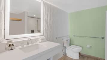 A modern bathroom with a white sink, a large mirror, a toilet, and a shower area.