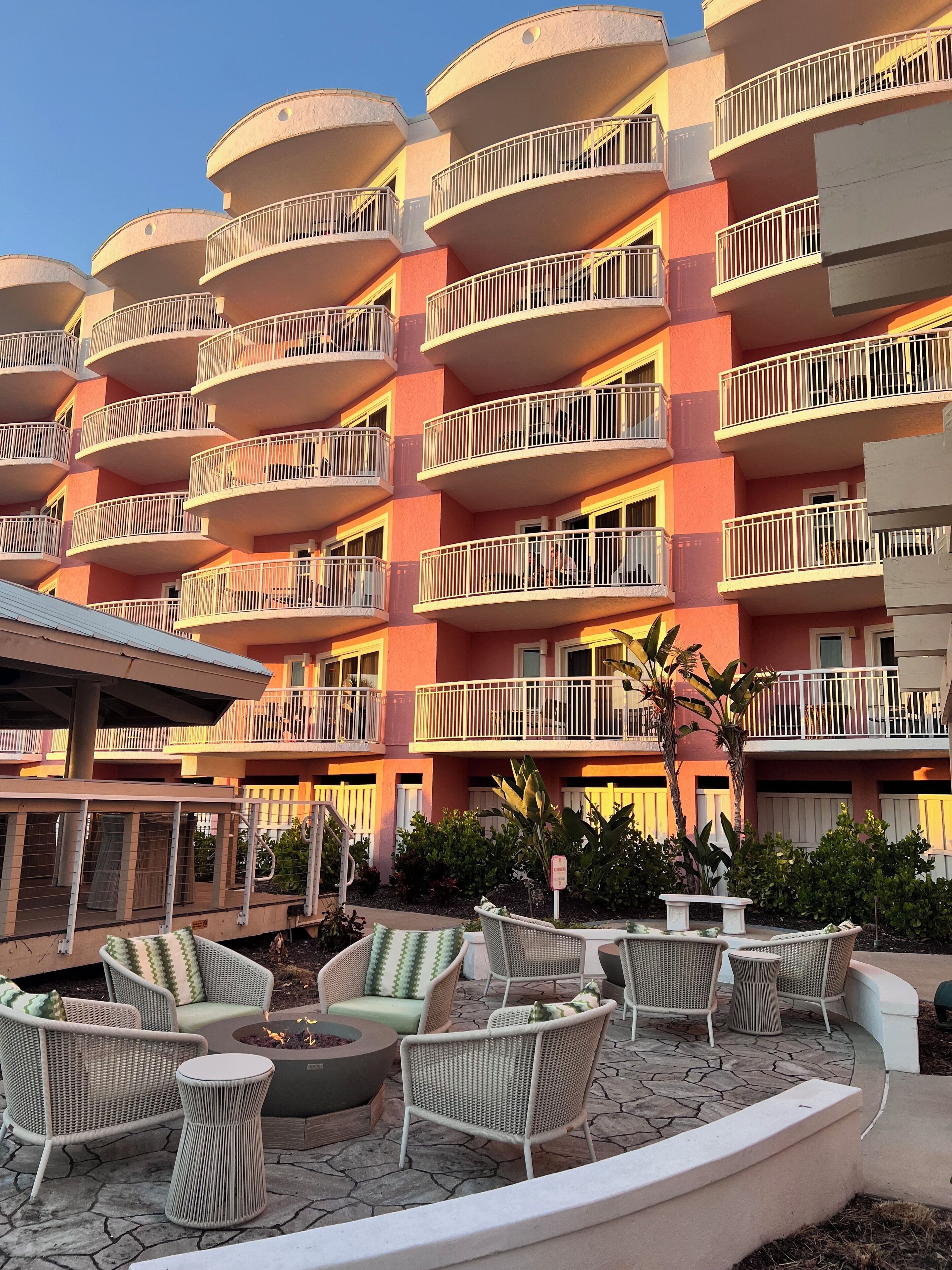 Et hotel med flere etager, altaner, udendørs siddepladser og et bålsted.
