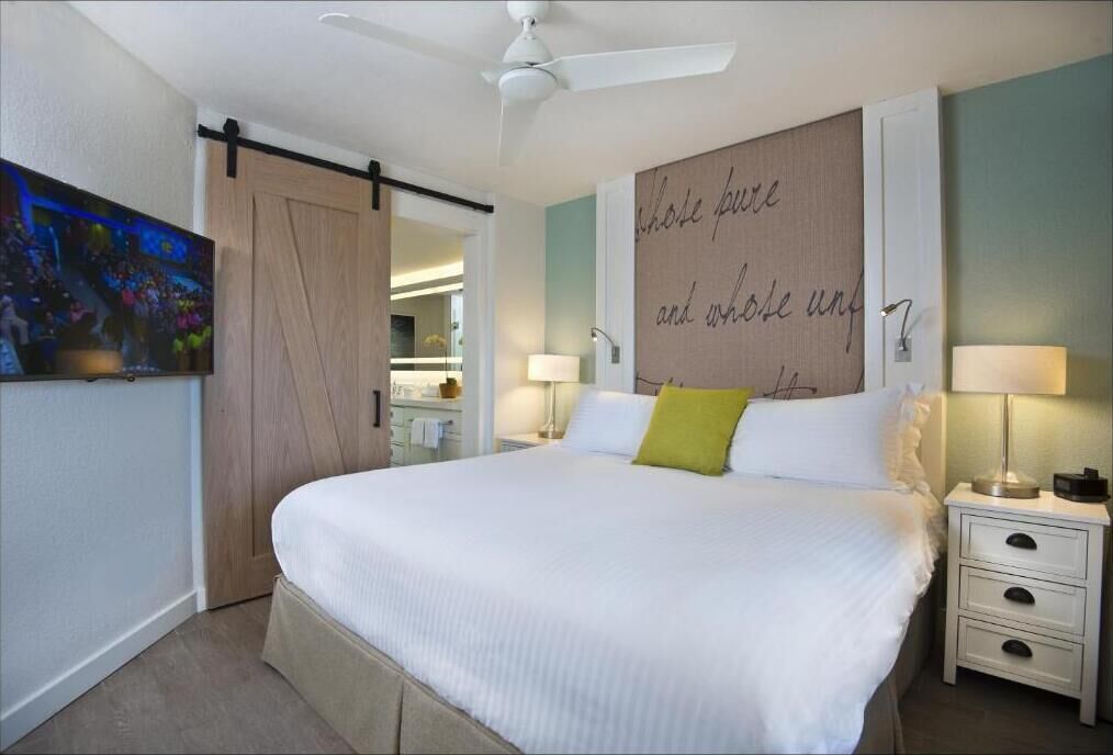 A bedroom with a bed, bedside tables, a ceiling fan, a wall with a motivational quote, and a TV on the wall.