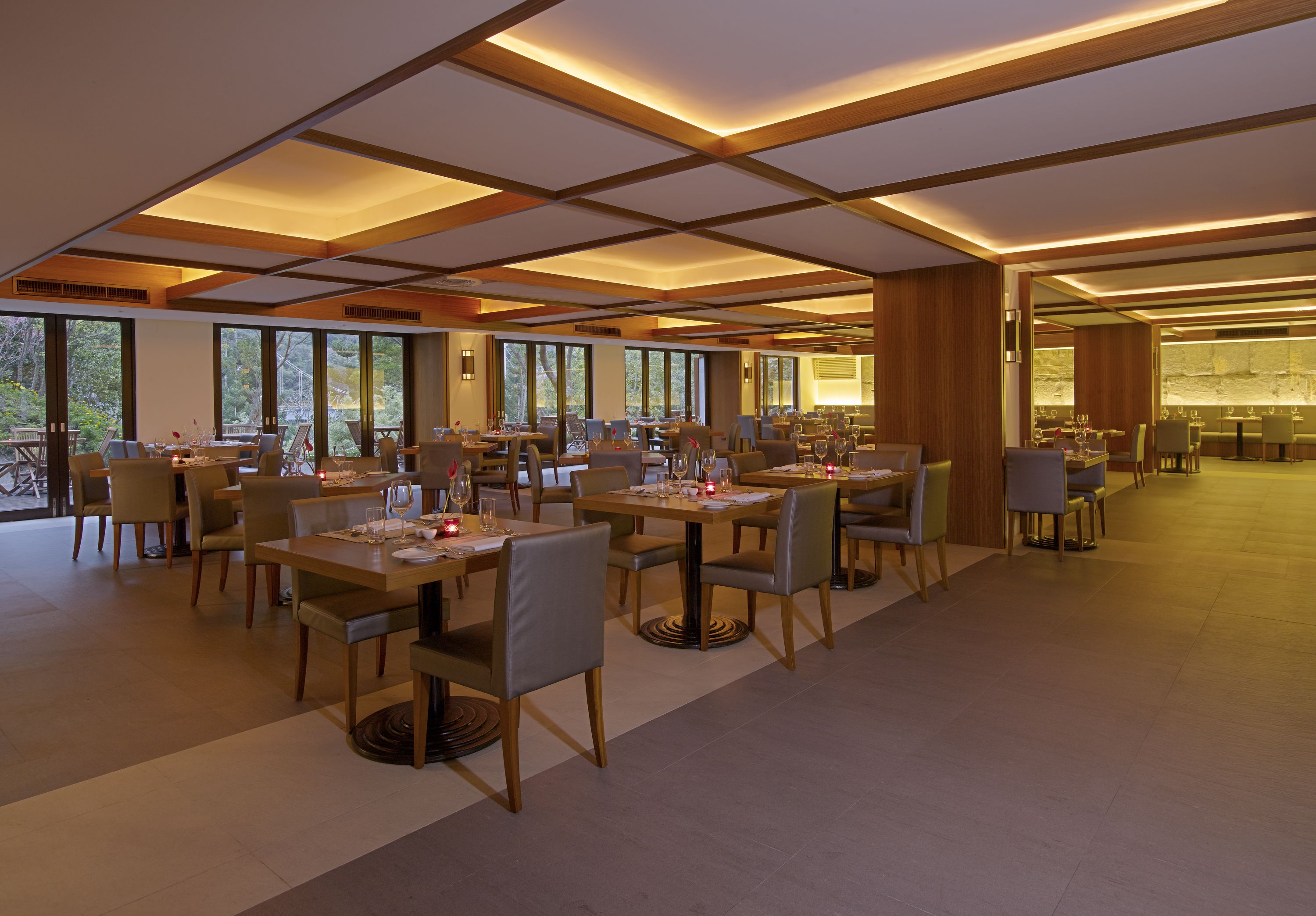 Un comedor amplio con varias mesas y sillas, ventanas grandes y un diseño moderno de techo.