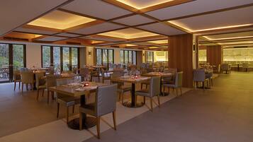 Un comedor amplio con varias mesas y sillas, ventanas grandes y un diseño moderno de techo.