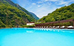 Una piscina con sillas de descanso, rodeada de exuberante vegetación y montañas.