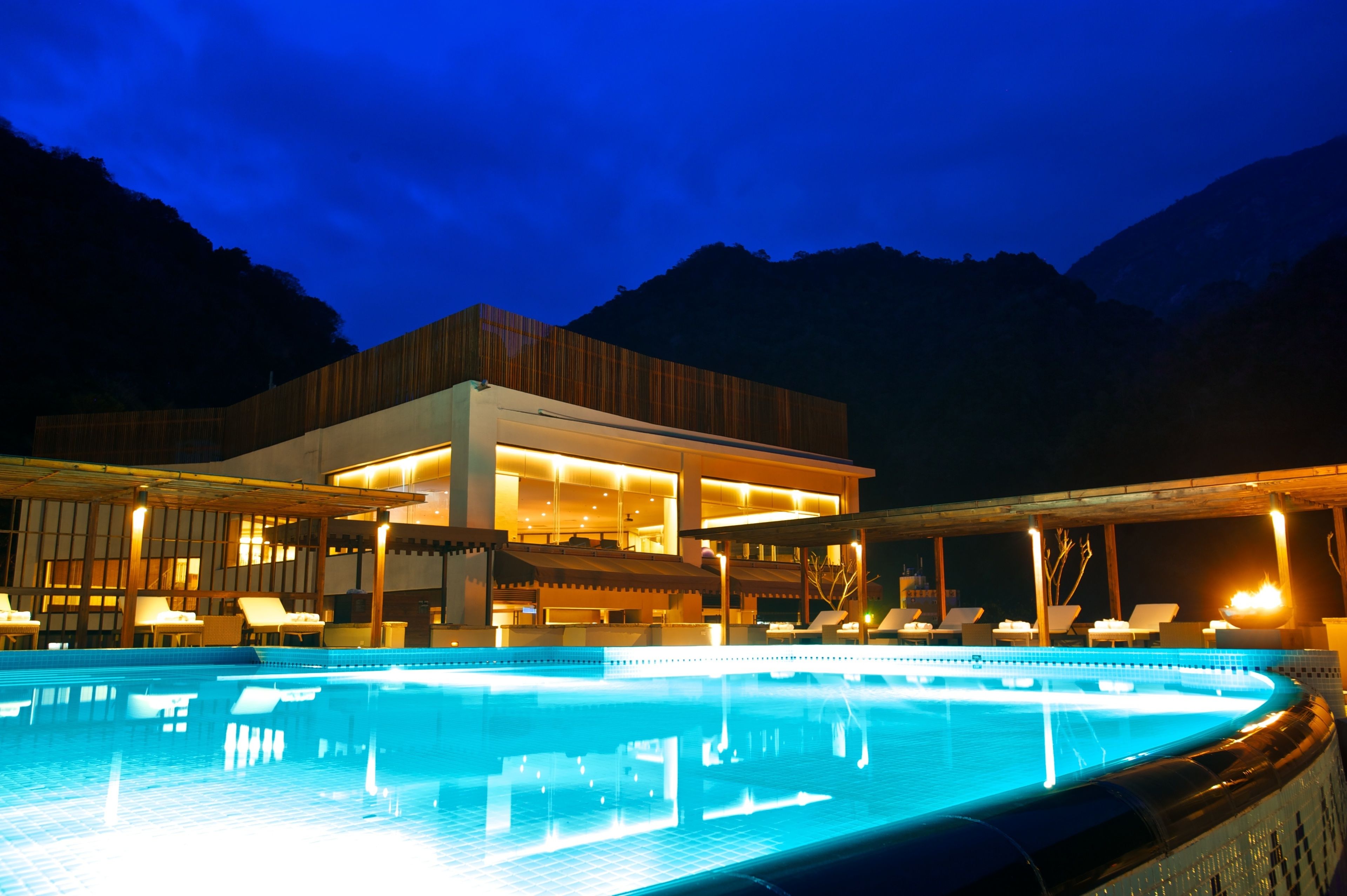 A modern hotel with a swimming pool, lounge area, and mountain views.