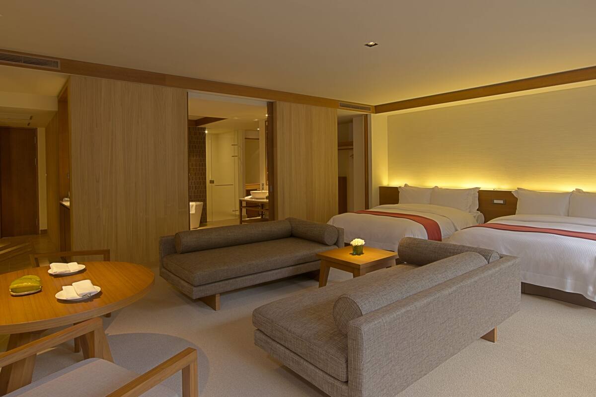 A hotel room with a bed, two sofas, a small table with a vase, and a dining table with plates and a bowl.