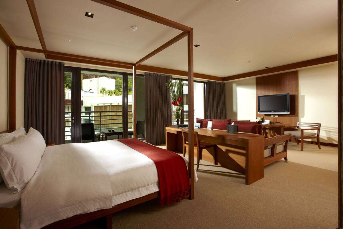 A hotel room with a large bed, a desk, a television, and a balcony with curtains.