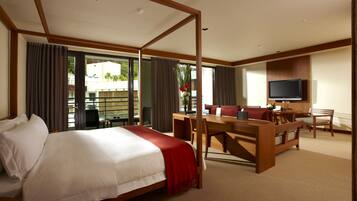 A hotel room with a large bed, a desk, a television, and a balcony with curtains.